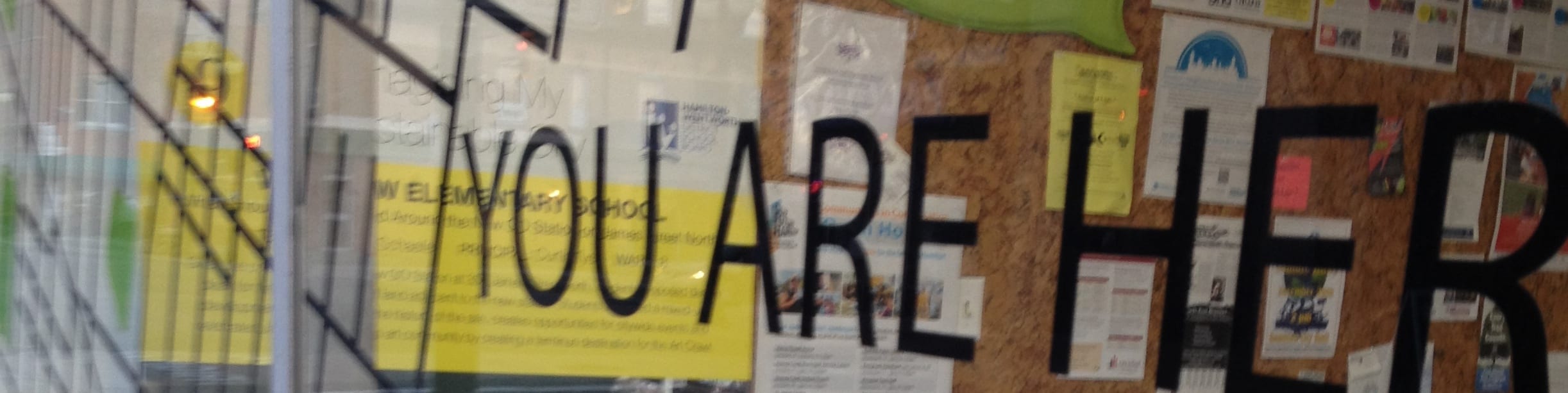 Photo of a glass wall with the words "you are here" beside a map.