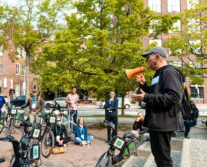 Person speaking into a megaphone, to a crowd or cyclists.