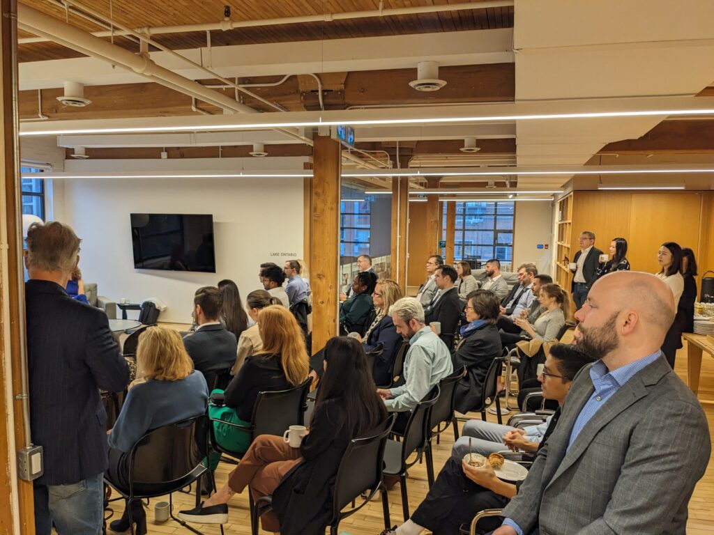 Photo of people sipping coffee and eating snacks while watching a presentation.